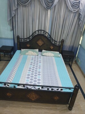 A bed with a patterned bedspread, a wooden headboard with decorative elements, and a window with curtains. - Chinese Guest House (Lahore)