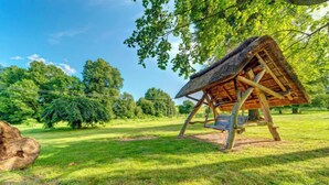 Eine rustikale Holzstruktur mit einem Reetdach, umgeben von üppigem Grün und Bäumen.