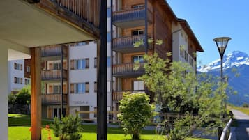 Un hôtel à plusieurs étages doté de balcons, d’un jardin fleuri et offrant une vue sur les montagnes en arrière-plan.