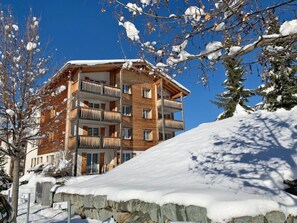 A multi-story wooden building with balconies, surrounded by snow-covered trees and a clear blue sky. - Surses Alpin by Interhome (Savognin)