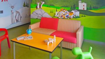Une pièce avec un canapé à rayures, une petite table sur laquelle se trouvent un globe terrestre et des livres, un fauteuil rouge et une fresque murale représentant un paysage de village.