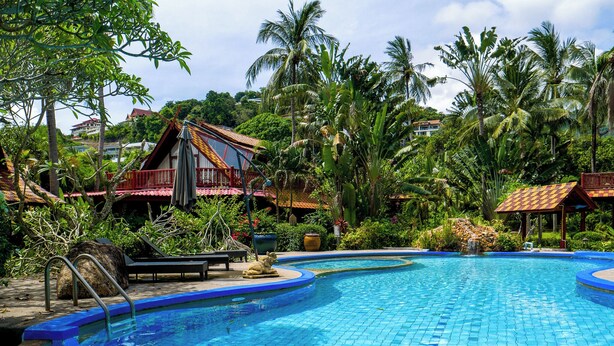 A swimming pool with a tiled edge, surrounded by lush greenery and palm trees. - Thai Style Wooden Beachfront Villa with Private Sala (Koh Samui)