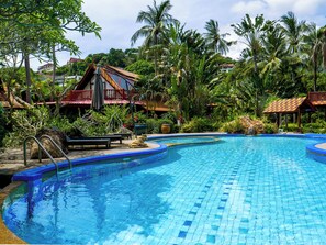 A swimming pool with a tiled edge, surrounded by lush greenery and palm trees.