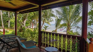 A covered outdoor seating area with wicker furniture, a small table, and a view of the beach and ocean. - Thai Style Wooden Beachfront Villa with Private Sala (Koh Samui)