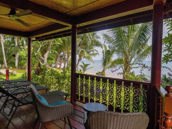 A covered outdoor seating area with wicker furniture, a small table, and a view of the beach and ocean.