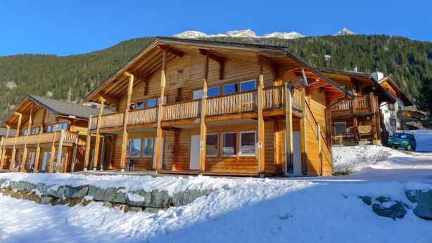 Un chalet en bois doté d’un balcon, situé au pied d’une montagne enneigée.