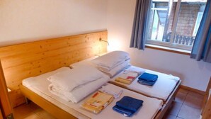 Un lit double avec du linge de lit et des serviettes blanches, une tête de lit en bois et une fenêtre avec des rideaux.