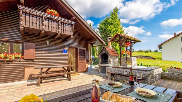 Un chalet rustique en bois, doté d’un four en pierre, d’une table de pique-nique et d’un espace de détente extérieur.