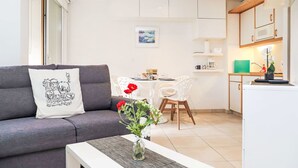A modern living room with a grey sofa, a white coffee table, and a vase with flowers. There is a dining area with a table and chairs, and a kitchen with white cabinets and appliances. - Mont-Fort 64 by Interhome (Siviez-Nendaz)
