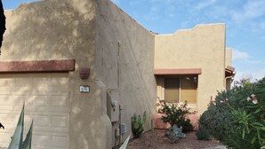 Ein zweistöckiges Gebäude mit sandfarbener Fassade, einer Garage und einem gepflegten Garten mit Kakteen und Sträuchern.