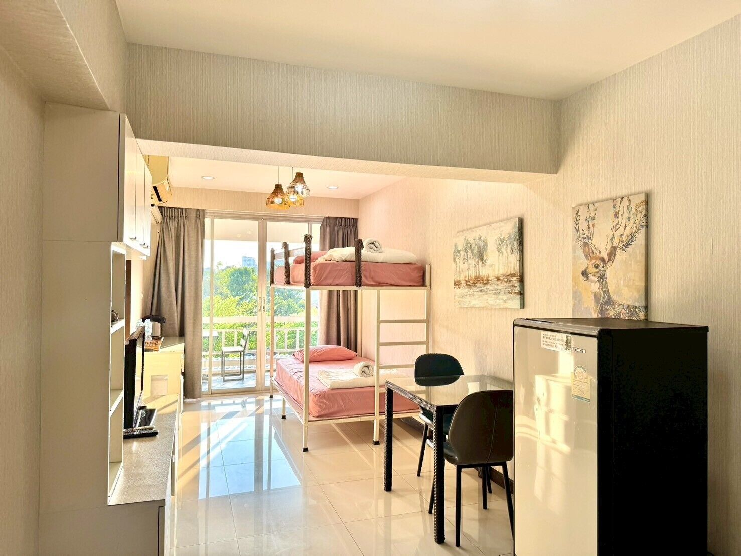 A hotel room with a bunk bed, a desk with a chair, a refrigerator, and artwork on the walls.