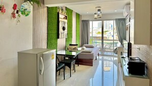 Eine moderne Wohnung mit Küche, Essbereich und Wohnzimmer. Sie verfügt über eine grüne Wand, ein großes Fenster mit Blick auf die Stadt und einen Balkon mit Gartenmöbeln.