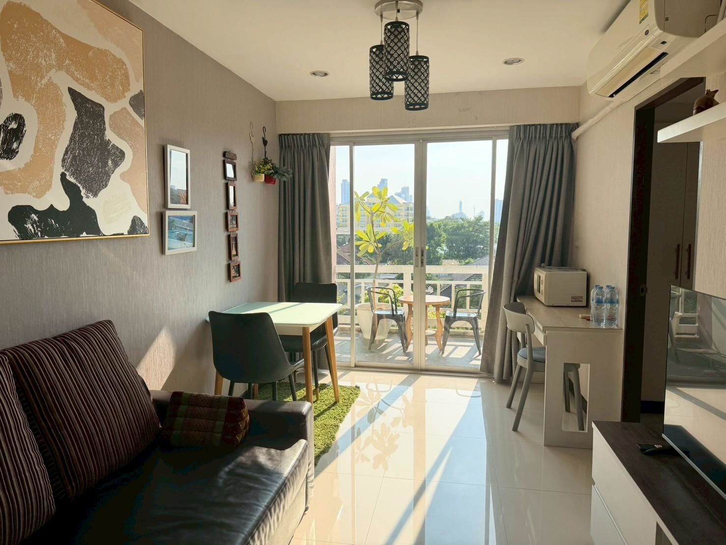 Un salon moderne comprenant un canapé, une table à manger et des chaises, un coin cuisine avec un four à micro-ondes, et un balcon offrant une vue sur la ville.