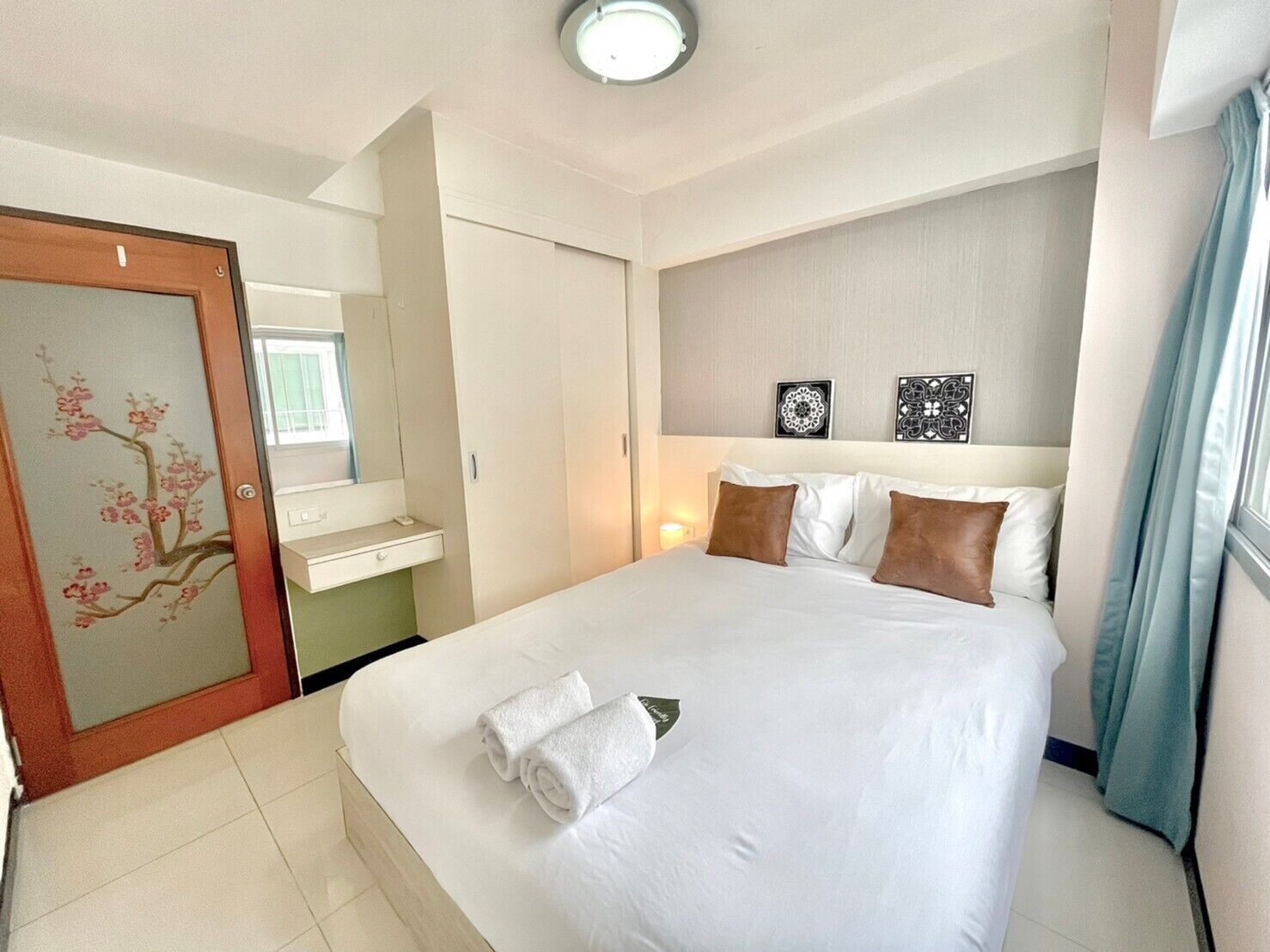 A hotel room with a large bed, a bedside table, a mirror, and a door with floral artwork.