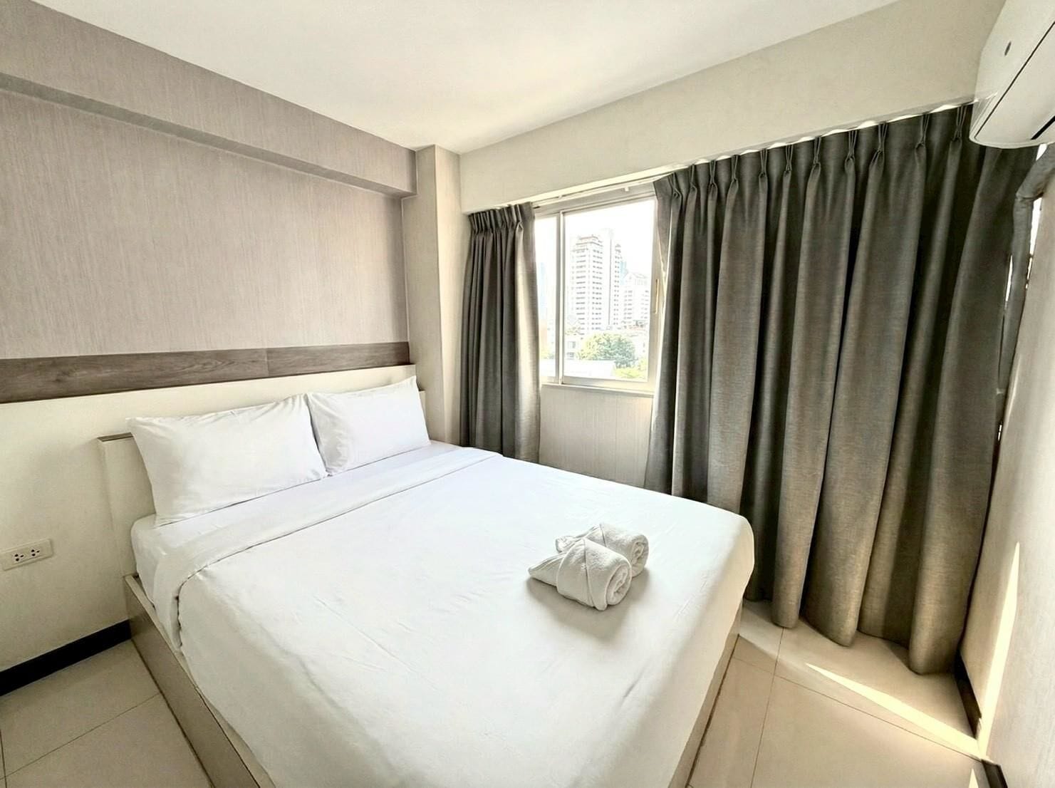 Une chambre d’hôtel avec un grand lit, une fenêtre avec des rideaux et une vue sur les bâtiments environnants.