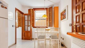 Una cocina con armarios blancos, una puerta de madera, una ventana con una lámpara colgante amarilla y una mesa de comedor con sillas.