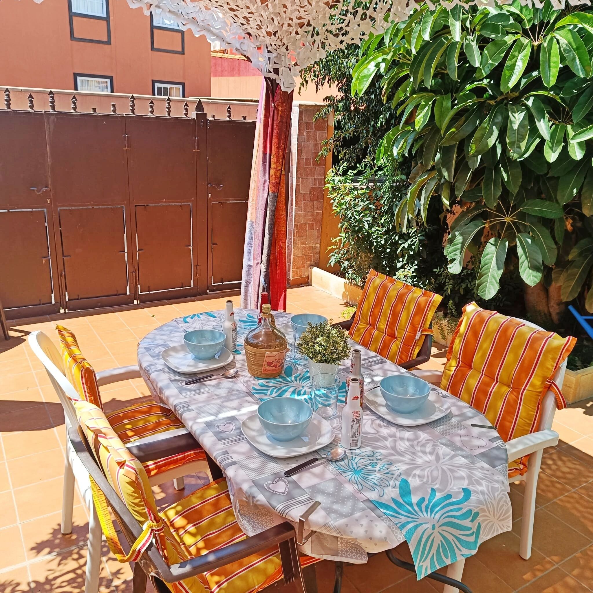 An outdoor patio with a table set for dining, surrounded by chairs with striped cushions.