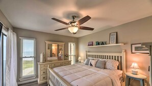 Un dormitorio con cama, mesita de noche, cómoda, ventilador de techo y ventana con persianas.