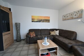 A living room with a brown sofa, a wooden coffee table, and a painting of a sunset on the wall.