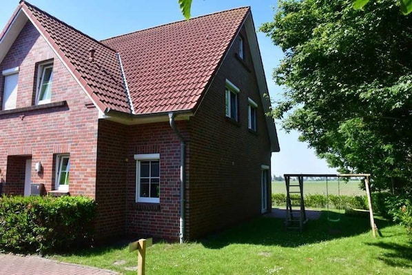 A two-story brick house with a red-tiled roof, a front porch, and a swing set in the yard.