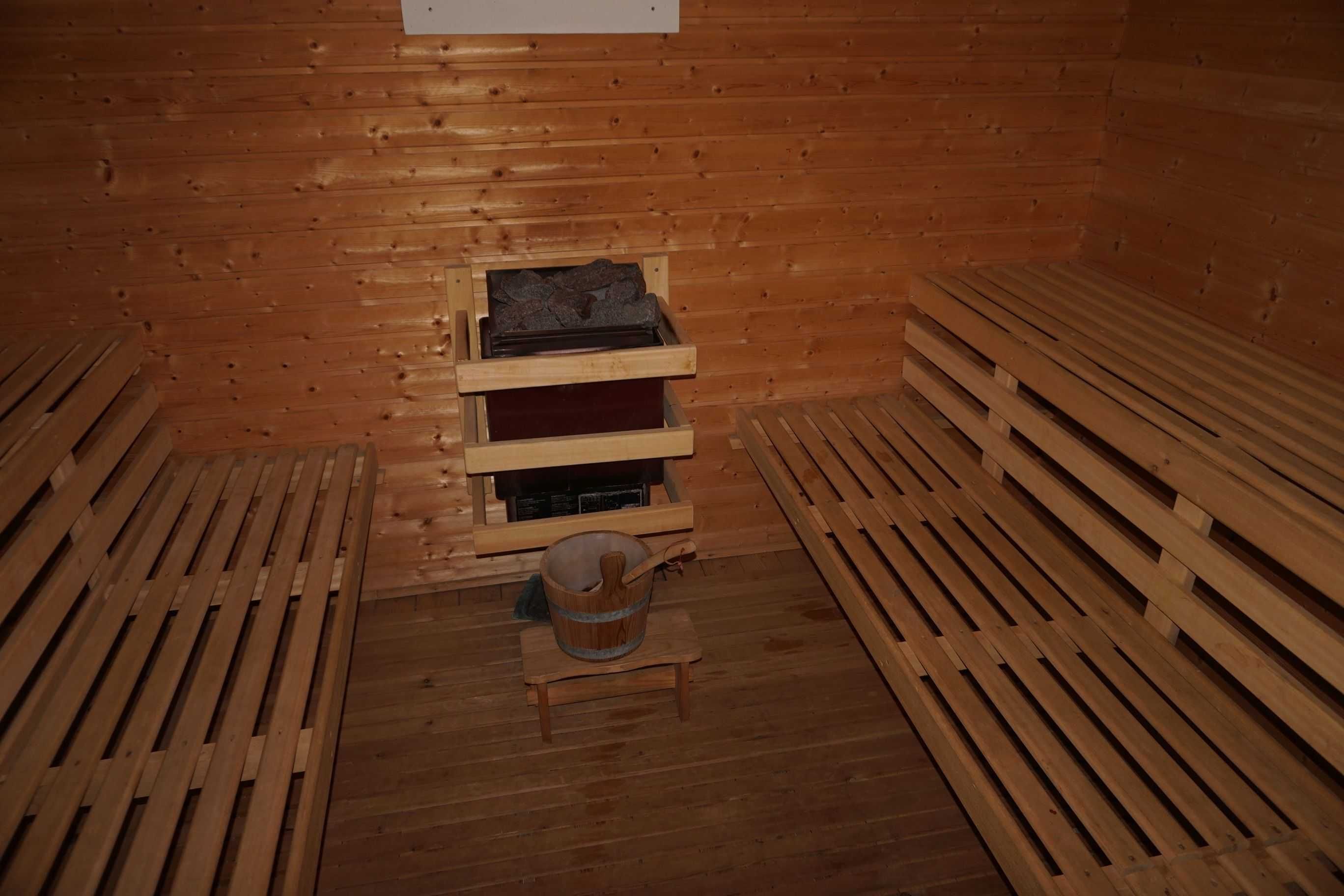 Ett basturum med träbänkar, en bänk med en hink och en hylla med en värmare.