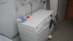 A compact laundry area with a front-loading washing machine, a dryer, and a small shelf with cleaning supplies. - sparrow's nest - vikingerhof (Wittmund)