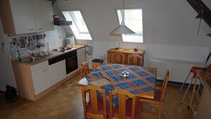 A kitchen with wooden cabinets, a dining table with a plaid tablecloth, and a window above the sink. - sparrow's nest - vikingerhof (Wittmund)