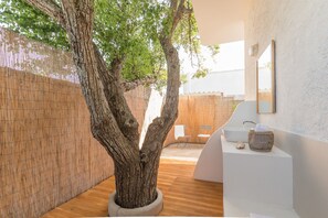 Une salle de bain moderne avec un grand arbre, un lavabo blanc et un miroir au mur.