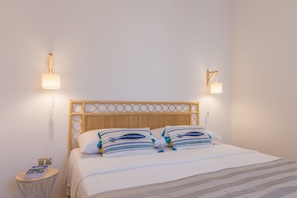 Un letto rifatto con lenzuola a righe, una testiera intrecciata e due lampade fissate al muro.