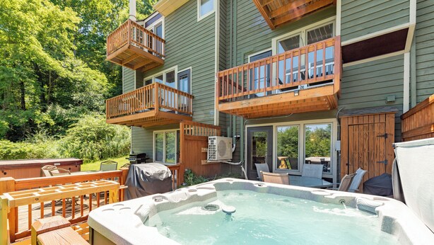 Een hottub in een achtertuin met houten terrassen en een balkon met meerdere niveaus.