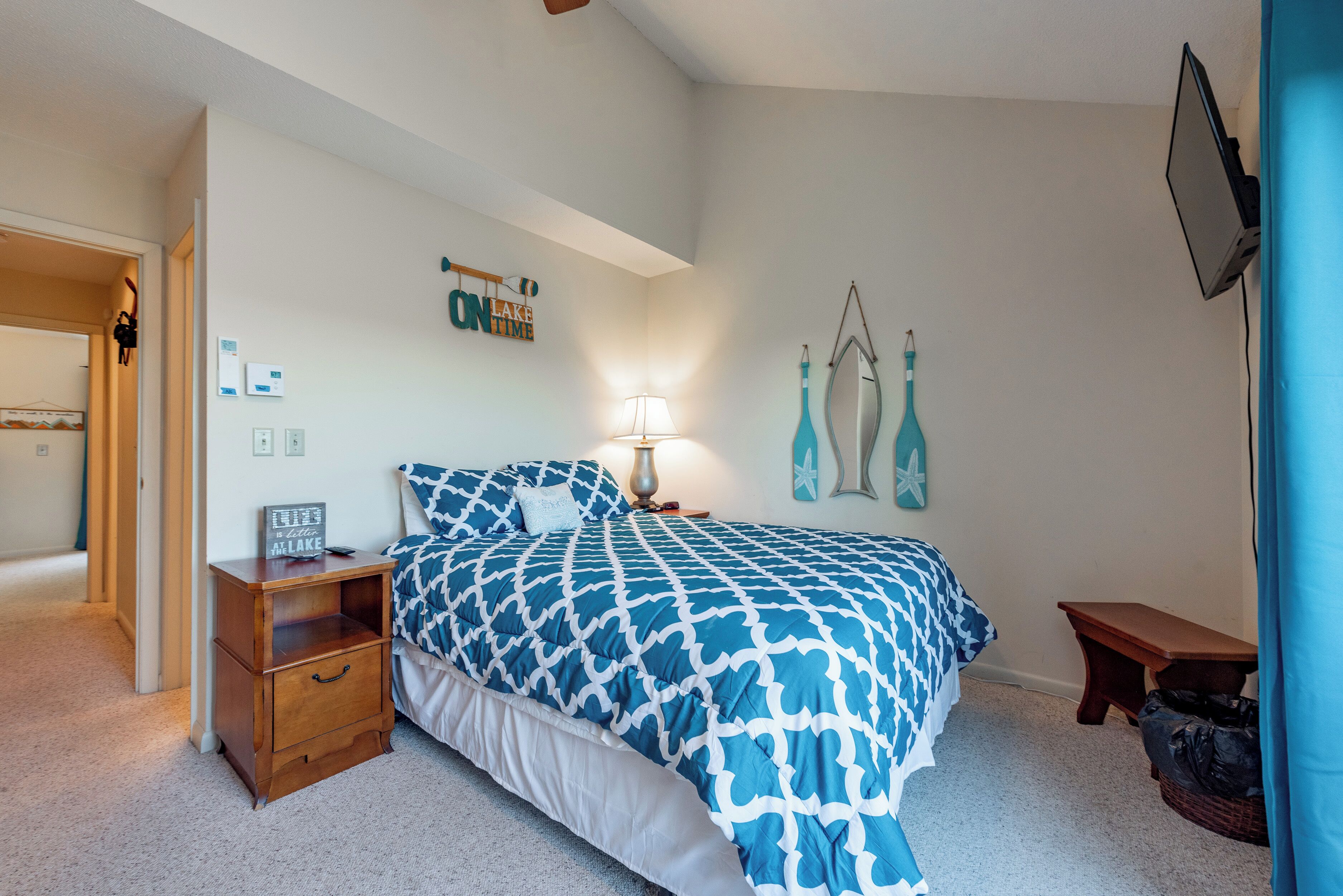 A bedroom with a bed, nightstand, lamp, and a wall sign.