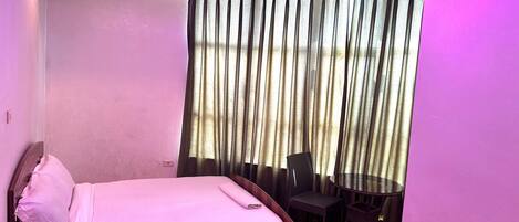 A hotel room with a bed, a small table with two chairs, and a window with curtains.