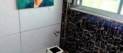 A bathroom with a marble floor, a black and white marble wall, a window, and a painting on the wall.