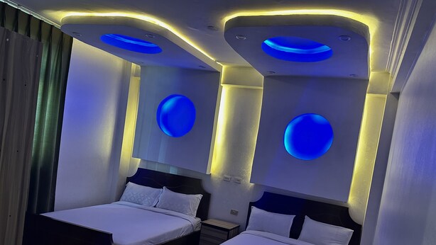A modern hotel room with two beds, a large rug, and unique ceiling lighting. - Addis Amba Guest House (Addis Ababa)