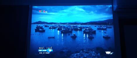 A projection of a coastal scene with boats on water, a cloudy sky, and a mountainous background.