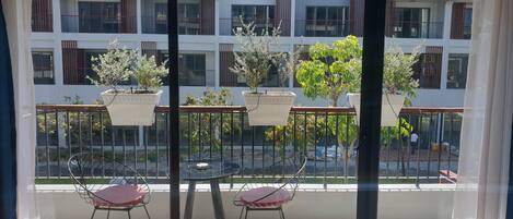 Un balcon avec deux chaises et des plantes en pot, donnant sur un immeuble doté de nombreux balcons.
