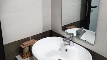 Une salle de bain avec un lavabo blanc, un miroir et un sèche-cheveux fixé au mur.