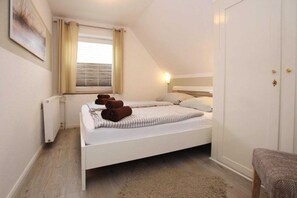 Une chambre à coucher avec un lit blanc, un radiateur, une fenêtre avec des rideaux et une lampe de chevet.