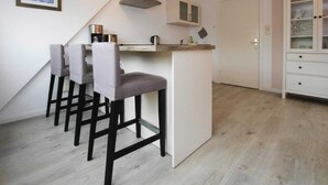 A compact kitchen with a central island, bar stools, a coffee machine, and a cabinet with glass doors. - Ferienwohnung, St. Peter-Ording (St. Peter-Ording)