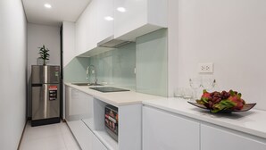A modern kitchen with white cabinetry, a stainless steel refrigerator, a built-in dishwasher, and a fruit bowl on the counter. - Narcissus Hotel and Apartment (Hanoi)