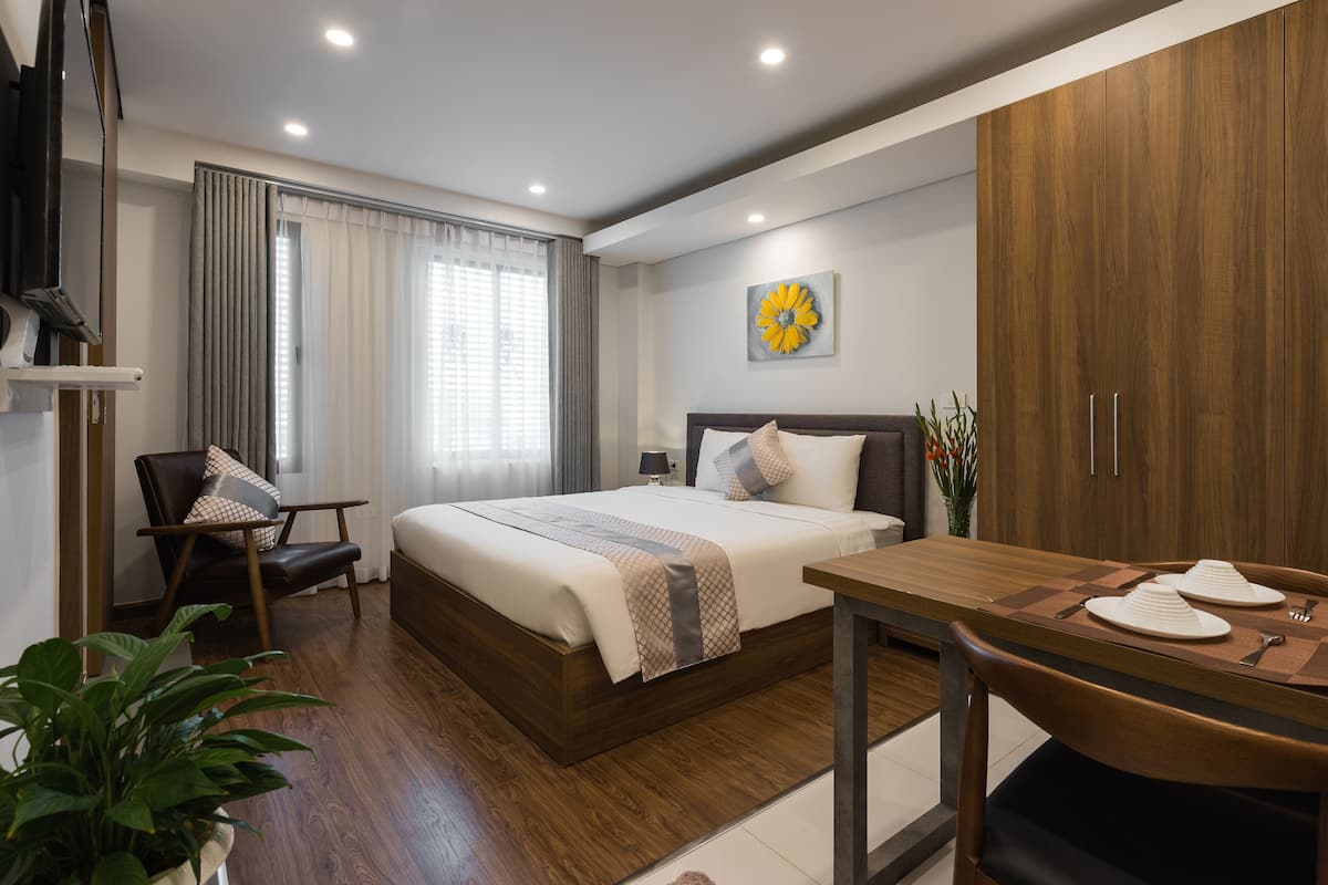 Ein modernes Hotelzimmer mit einem großen Bett, einem Holzschrank, einem Esstisch mit Stühlen und einer Topfpflanze.