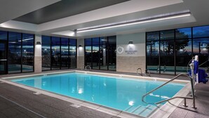 An indoor swimming pool with clear markings, a lifeguard sign, and a view of the parking lot outside.