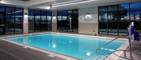 An indoor swimming pool with clear markings, a lifeguard sign, and a view of the parking lot outside.