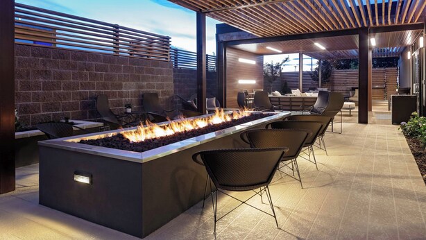 An outdoor patio with a fire feature, seating, and a brick wall.