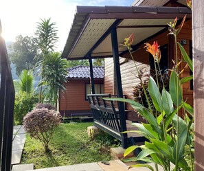 A wooden house with a porch, surrounded by lush greenery and a small garden. - Guesthouse 88 (Phang Nga)