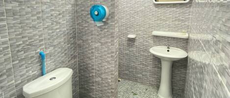 A bathroom with a toilet, bidet, and sink, tiled with a gray pattern.
