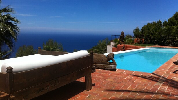 A wooden bench overlooking a swimming pool with a view of the ocean.