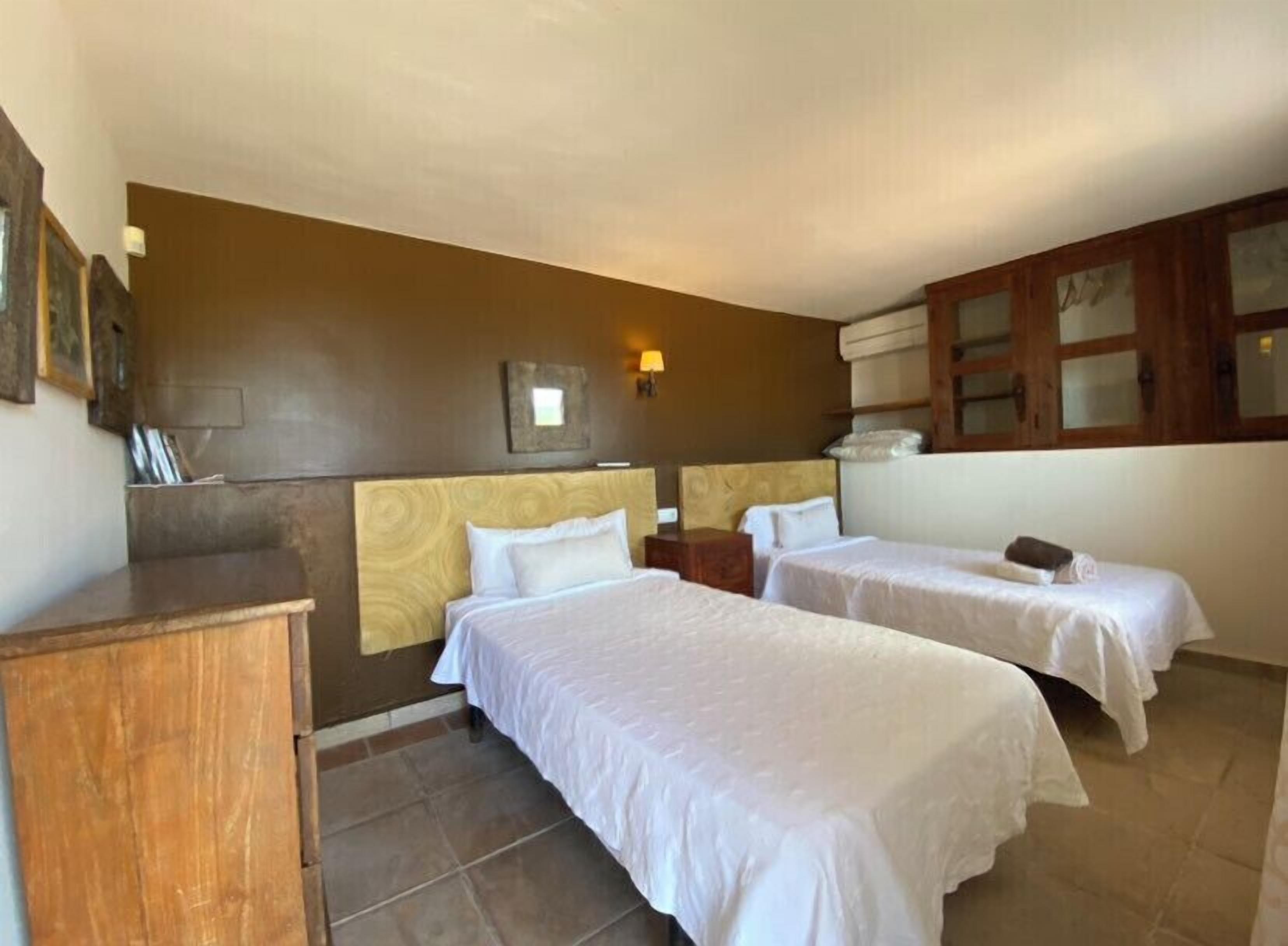 Una habitación de hotel con dos camas individuales, un aparador de madera, una mesita pequeña y una lámpara fijada a la pared.