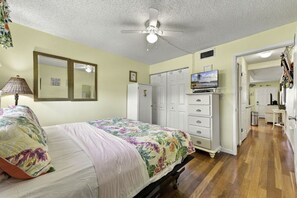 Une chambre à coucher comprenant un lit, une commode, un téléviseur et un ventilateur de plafond.