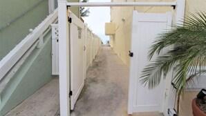A narrow alleyway with a white gate, a palm tree, and a concrete path.